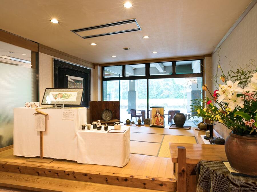 A traditional Japanese room with tatami flooring, a wooden stage with a display, and a large window with a view of greenery.