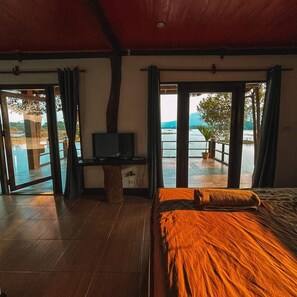 Un dormitorio con cama, escritorio y televisor, y vista a un lago a través de amplias puertas correderas.