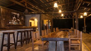 Un coin bar au style rustique, avec des tabourets en bois et une longue table en bois, entouré de poutres en bois et agrémenté de luminaires suspendus.
