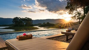 Un salon de bord de piscine offrant une vue sur un coucher de soleil se reflétant sur un lac et des montagnes.