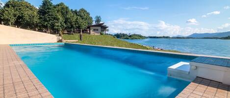 A swimming pool with a clear blue water, surrounded by a tiled deck, and a view of a lake and mountains in the background.