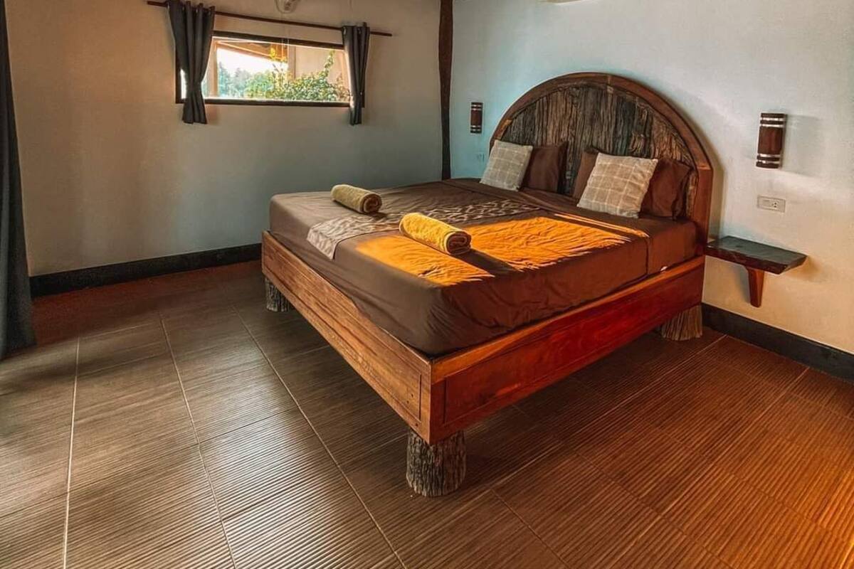Un dormitorio amplio con una cama grande, cabecera de madera y una ventana con cortinas.