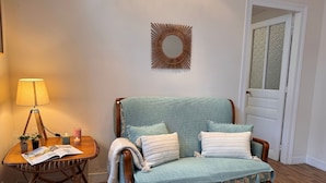 A cozy room with a wooden floor, a green sofa with cushions, a small wooden side table with a lamp, and a decorative mirror on the wall. - Beautiful private villa for 2 guests with WIFI, TV and terrace (Cancale)