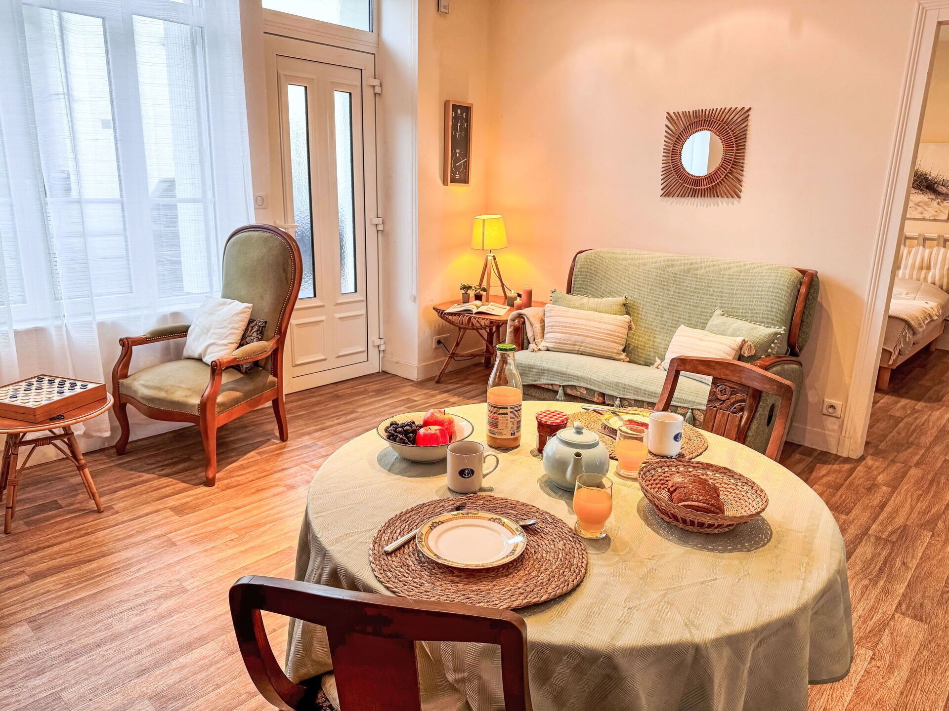 Uma sala de jantar acolhedora com uma mesa redonda posta para dois, um sofá verde e uma cadeira de madeira.