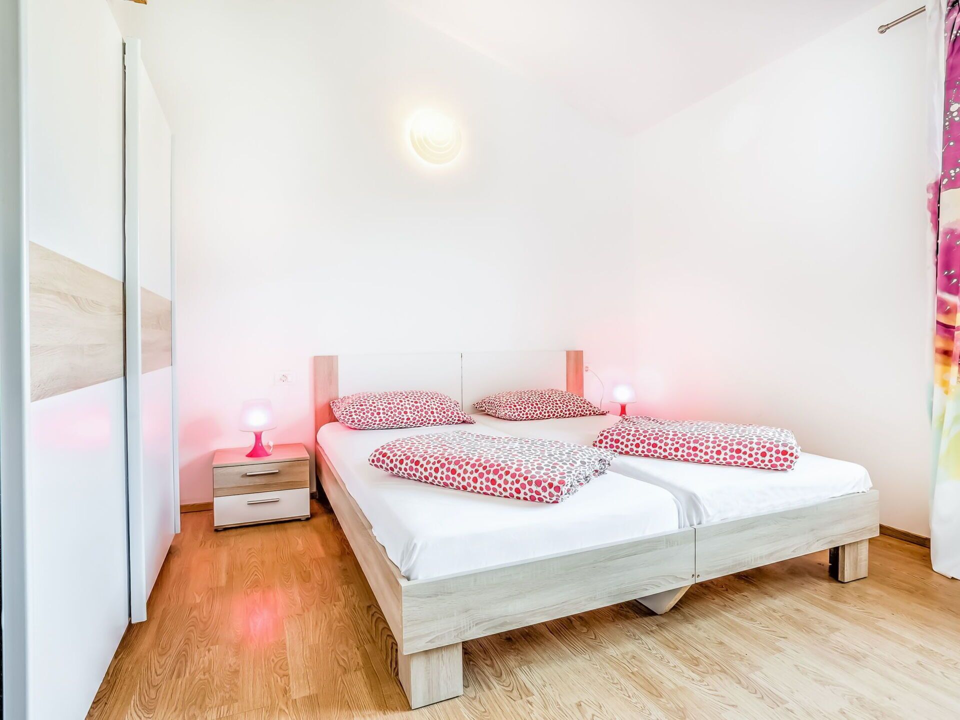 A bedroom with a double bed, two bedside tables with lamps, and a wooden floor.