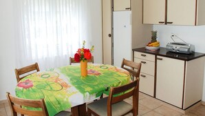 A small kitchen with a dining table, chairs, a refrigerator, and a radio.
