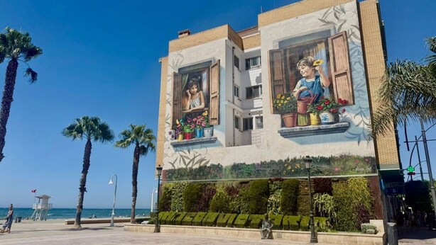 A building with a mural of a child and flowers, palm trees, and a clear sky.