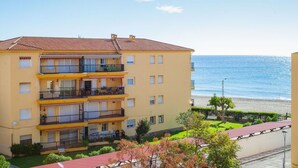 A multi-story yellow building with balconies, a beach view, and a clear sky.