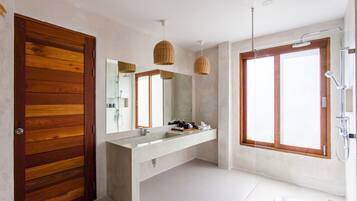 Un baño moderno con puerta de madera, un espejo grande, tocador con lavabo y zona de ducha.