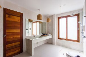 Un baño moderno con puerta de madera, un espejo grande, tocador con lavabo y zona de ducha.