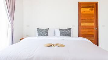 Een net opgemaakt bed met witte lakens en twee gestreepte kussens, een houten deur en een raam met gordijnen.