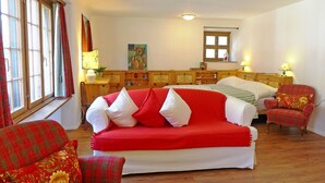 Une pièce avec un canapé rouge, un lit en bois, une chaise et une fenêtre avec des rideaux.