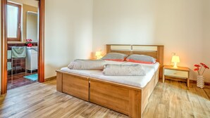 A bedroom with a wooden bed, two bedside tables with lamps, a bathroom visible through an open door, and a tiled floor. - Lovely apartment for 2 guests with pool, WIFI, A/C, TV and pets allowed (Umag)