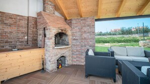 An outdoor kitchen area with a brick oven, a sink, and wicker furniture. - Lovely apartment for 2 guests with pool, WIFI, A/C, TV and pets allowed (Umag)