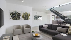 Ein modernes Wohnzimmer mit einer Couch, Sesseln und einem Couchtisch. Eine Treppe führt zu einer oberen Ebene.