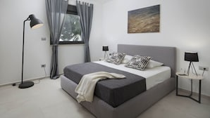 Ein modernes Schlafzimmer mit einem großen Bett, grauen Vorhängen, einem Bild an der Wand und zwei Nachttischlampen.