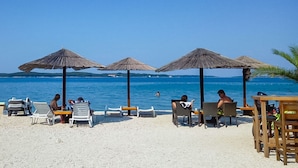 Ein Strand mit Liegestühlen und Sonnenschirmen, einem klaren blauen Himmel und dem Meer im Hintergrund.