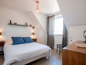 A bedroom with a large bed, a desk, a chair, a hanging light fixture, and a window with curtains.