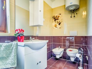 Ein modernes Badezimmer mit einem weißen Waschbecken, einem Bidet und einer Toilette. Auf dem Waschbeckenbrett steht eine rote Blumenvase.