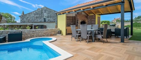 A backyard with a swimming pool, outdoor seating, and a stone building.