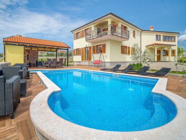 Ein Pool mit Liegestühlen, eine überdachte Lounge und ein zweistöckiges Gebäude mit Balkonen.