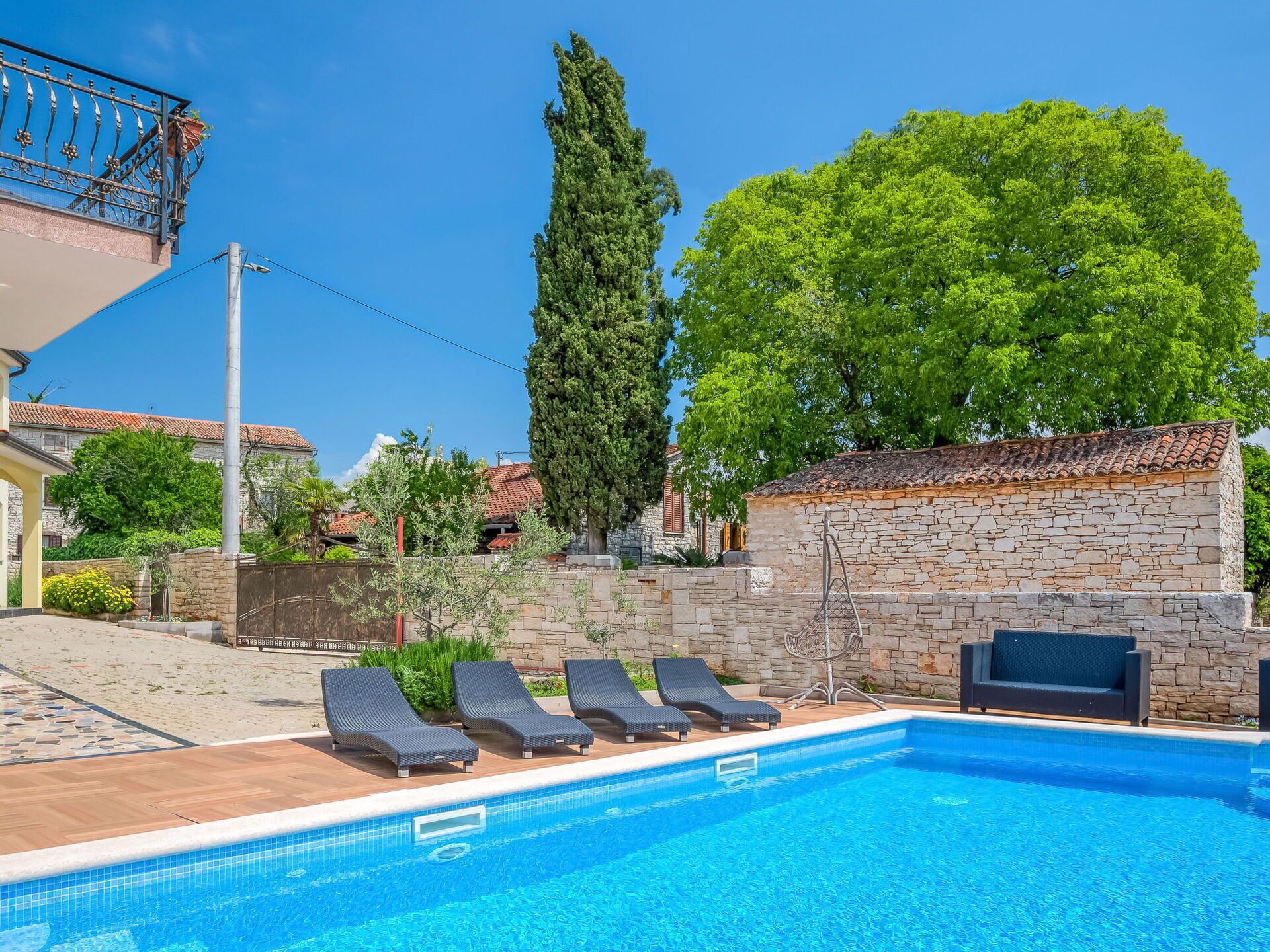 A swimming pool with lounge chairs, a stone wall, and a tree.