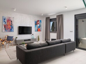 Ein modernes Wohnzimmer mit einem grauen Sofa, einem Flachbildfernseher, abstrakter Kunst und einem Fenster mit Vorhängen.