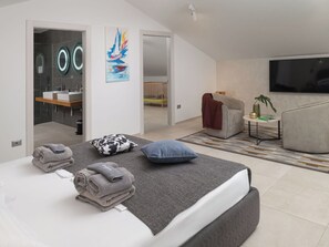A modern bedroom with a bed, a TV, a sofa, and a bathroom with a shower.