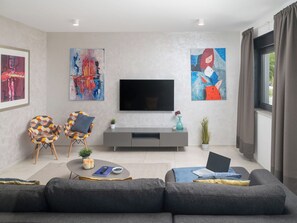A modern living room with a grey sofa, a coffee table, a flat-screen TV, and abstract paintings on the walls.