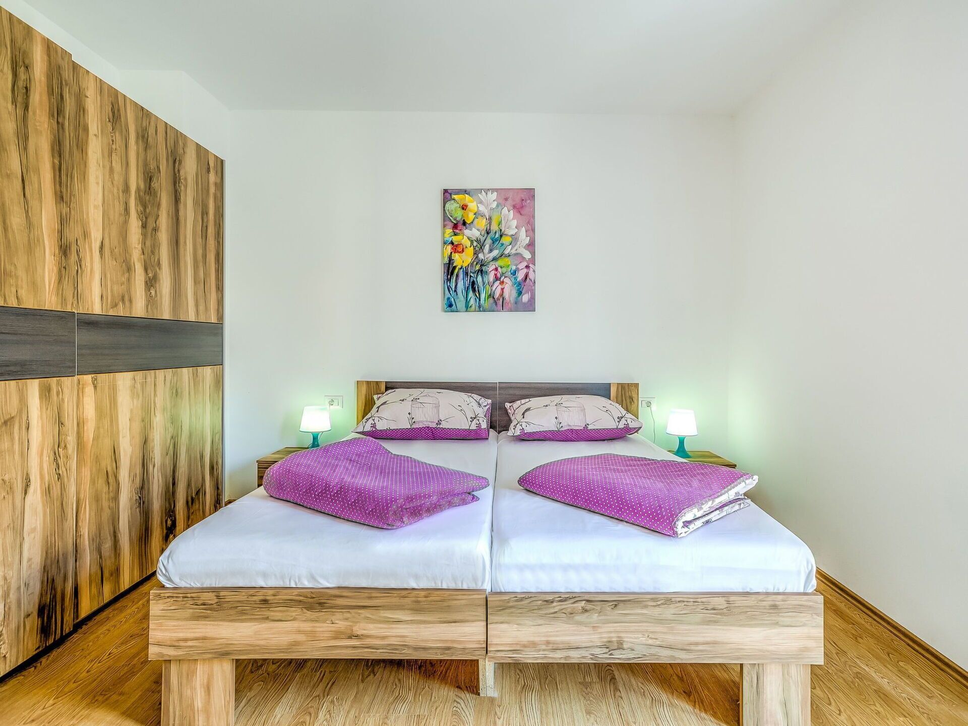 Una cama doble con dos almohadas, una mesita de noche con lámpara y un armario de madera.