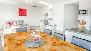 A modern living room with a wooden dining table, a sofa, and a kitchen area with a microwave.