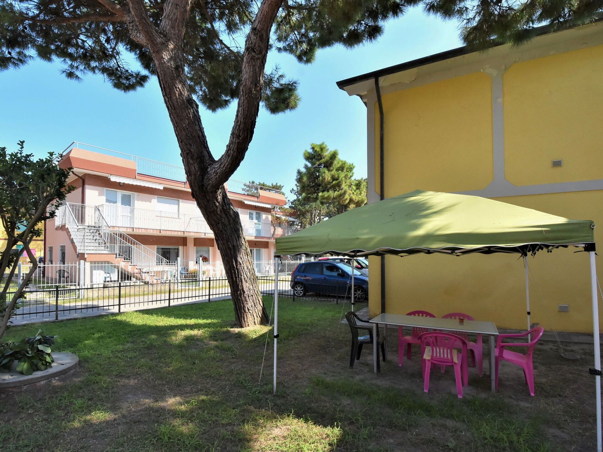 Un edifici groc amb una zona d'estar a l'aire lliure coberta i un arbre al primer pla.
