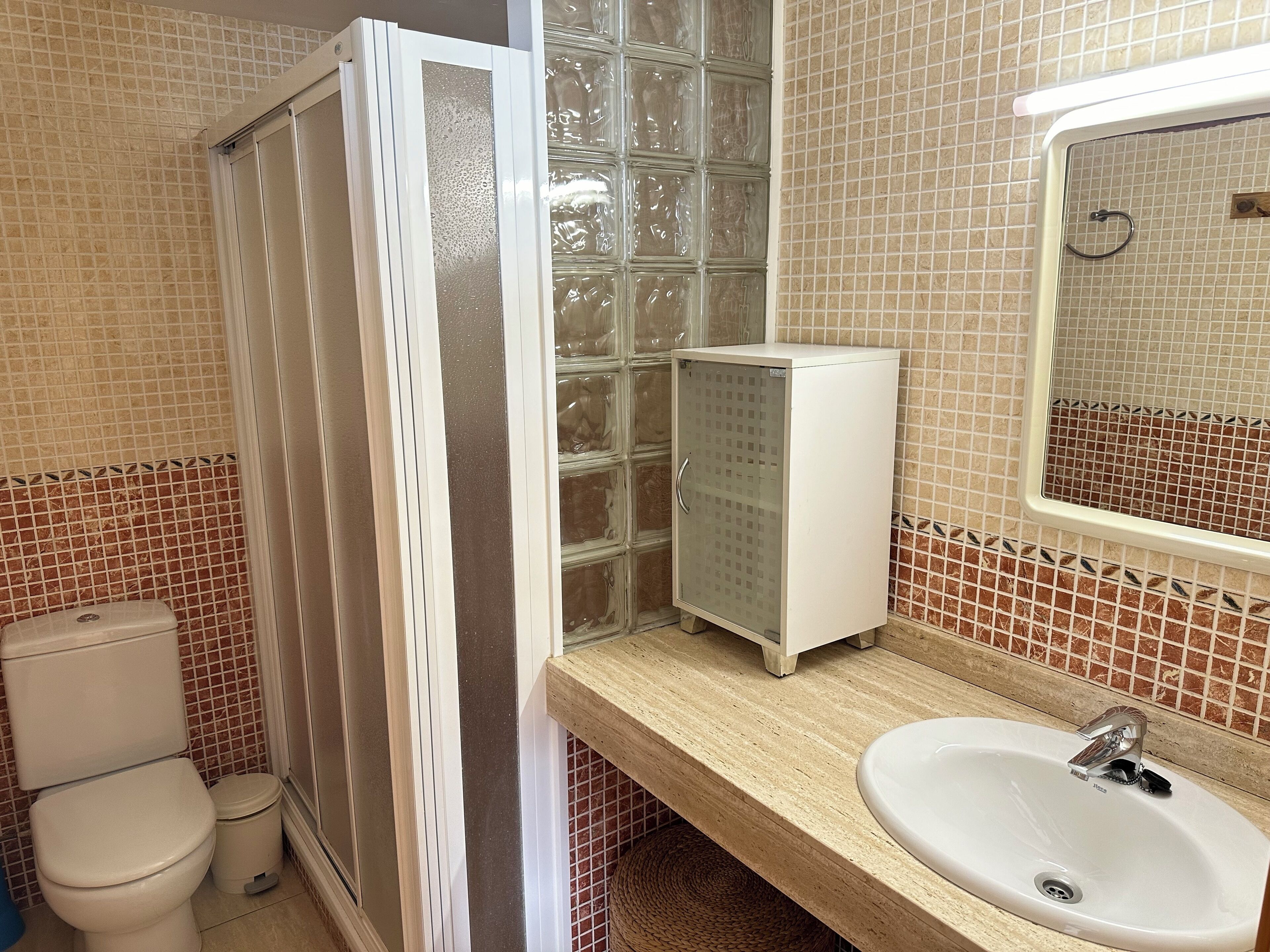 Un baño con inodoro, cabina de ducha, lavabo y espejo.