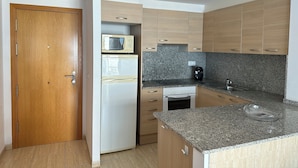 A compact kitchen with wooden cabinets, a built-in microwave, a refrigerator, and a granite countertop. - Agi Norfeu Park 24 Apartamento for rent in Roses Girona. (Rosas / Roses)