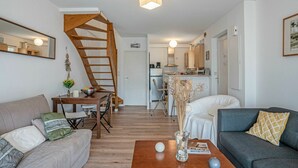 A modern living room with a wooden staircase, a dining area, and a kitchen in the background. - Stunning  villa for 4 people with WIFI, TV, terrace and pets allowed (Mimizan)