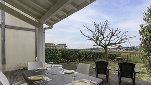 An outdoor patio with a table set for four, surrounded by chairs, under a covered area with a view of a tree and distant buildings. - Stunning  villa for 4 people with WIFI, TV, terrace and pets allowed (Mimizan)