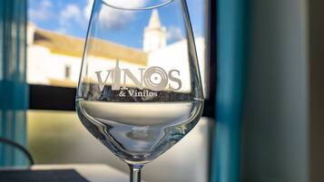 A wine glass with the inscription "VINOS & Vinilos" on it, placed in front of a window with a view of a building and a clear sky.