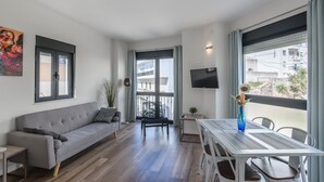 Een moderne woonkamer met een grijze bank, een eettafel en een televisie aan de muur.