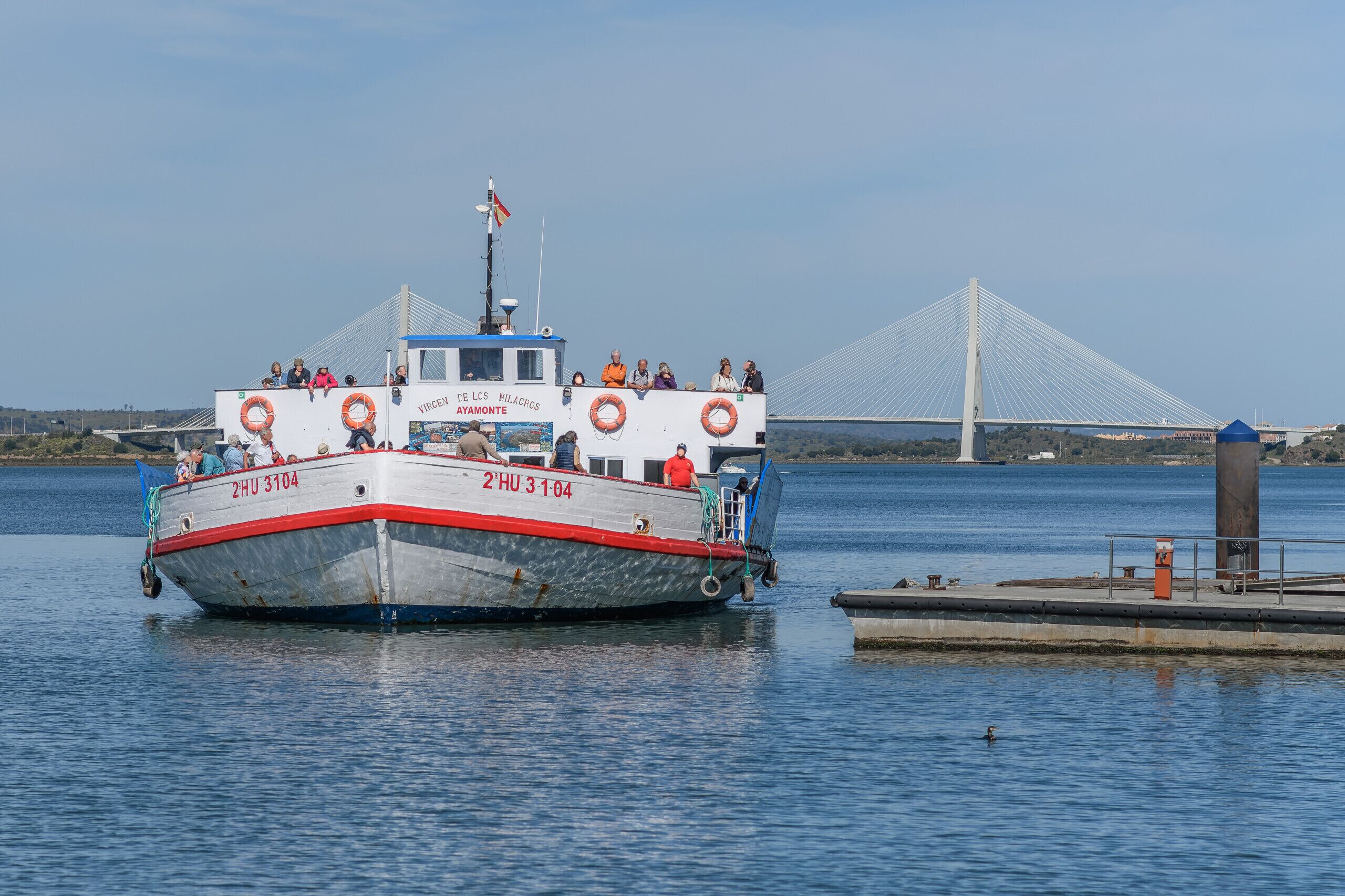 Un bateau avec des personnes à bord, amarré près d’un pont et d’une jetée.