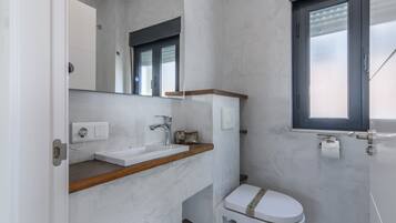 Un baño con lavamanos blanco, espejo, inodoro y ventana.