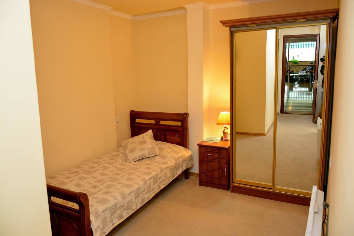 A small bedroom with a bed, a nightstand, a mirror, and a door leading to a hallway.