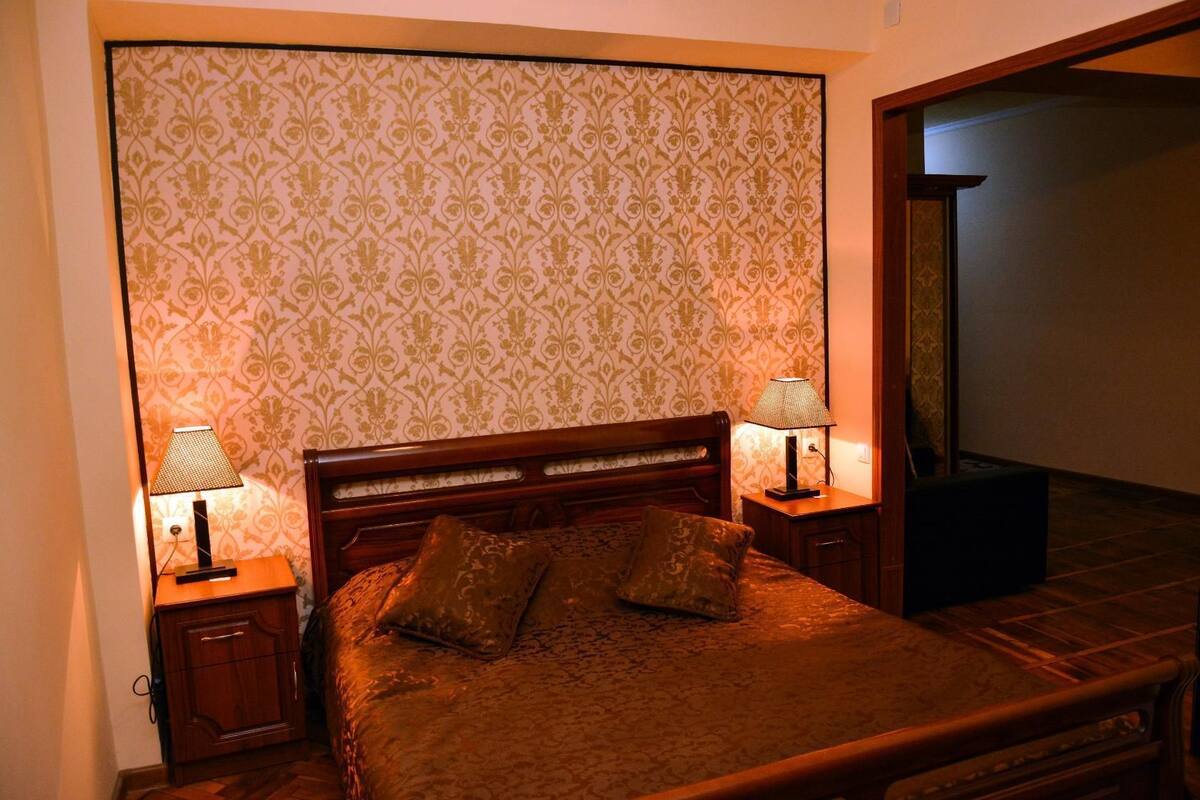 A neatly made bed with a wooden headboard, two bedside tables with lamps, and a patterned wallpaper.