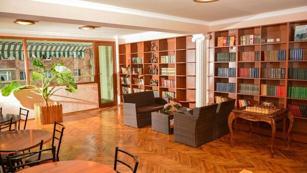 A library with wooden floors, bookshelves, a chess table, and a dining area with chairs and a table. - Sanahin Bridge Hotel (Alaverdi)