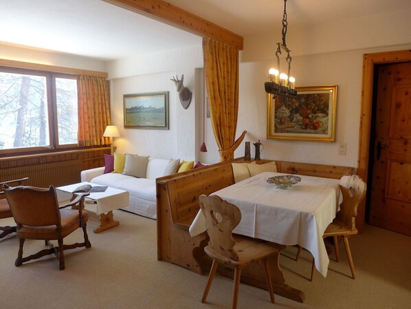 A cozy room with a wooden bench, a table with a white tablecloth, a sofa, and a painting on the wall.