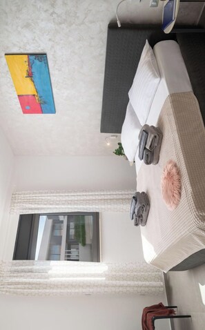 A room with a bed, a window with curtains, a painting on the wall, and a power outlet.