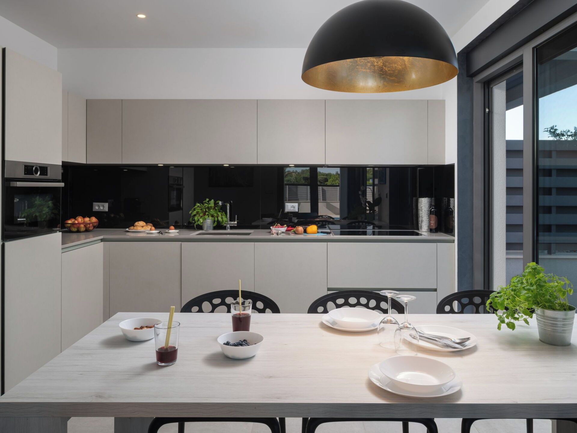 Una cocina moderna con comedor, que cuenta con una isla grande, lámparas colgantes negras y vistas al exterior.