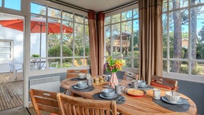 Un comedor luminoso con una mesa redonda de madera, sillas y vistas a una terraza de madera y árboles.