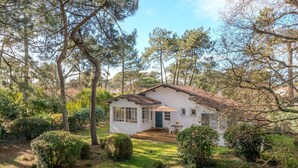 Una casita blanca de techo de tejas, rodeada de árboles y arbustos.