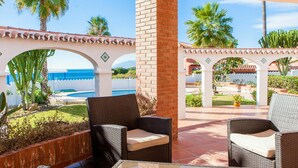 Un patio con mobiliario de mimbre, una mesa de vidrio y vista al océano.