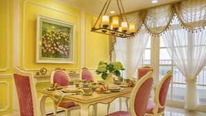 Une salle à manger avec un mur jaune, un grand tableau représentant des motifs floraux et un lustre.